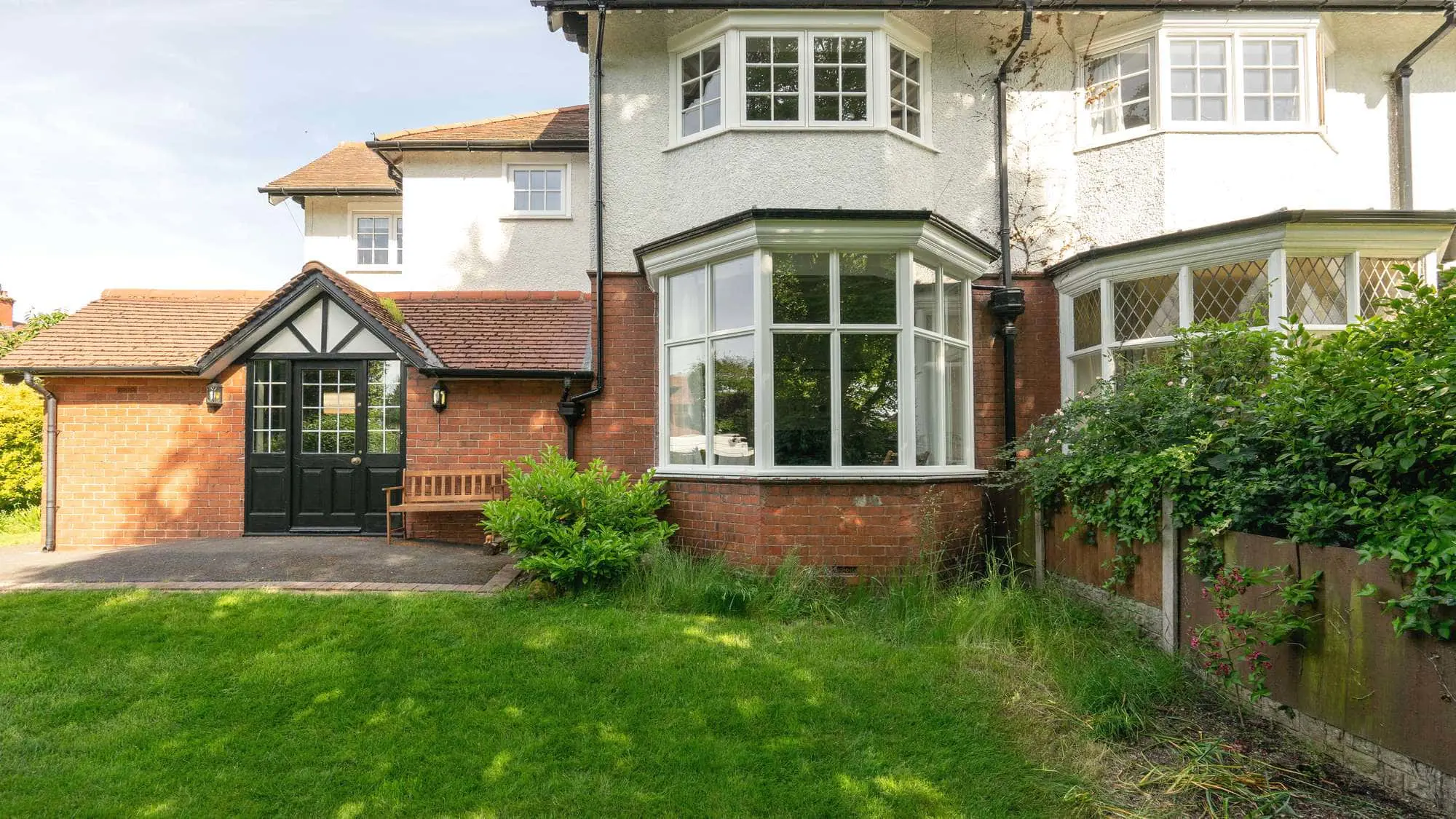 Wide angle view showing front of house with timber bay window on the ground floor, and UPVC timber alternative windows to the second floor.