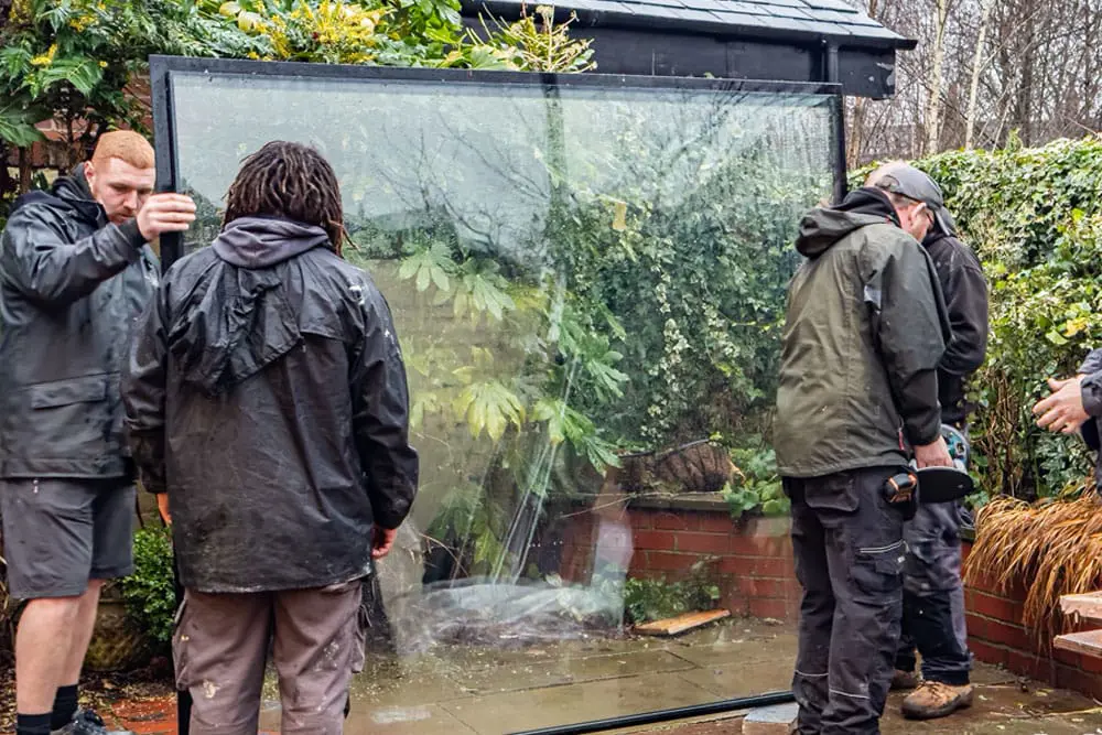 Installers lifting a large piece of glass into place.